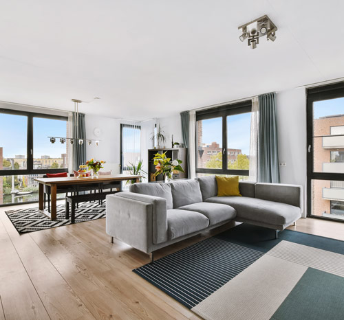 Bright, modern living room with a grey sofa, dining area, and large windows.