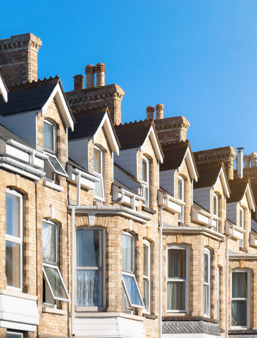 Row of well-maintained Victorian houses with chimneys under a clear blue sky